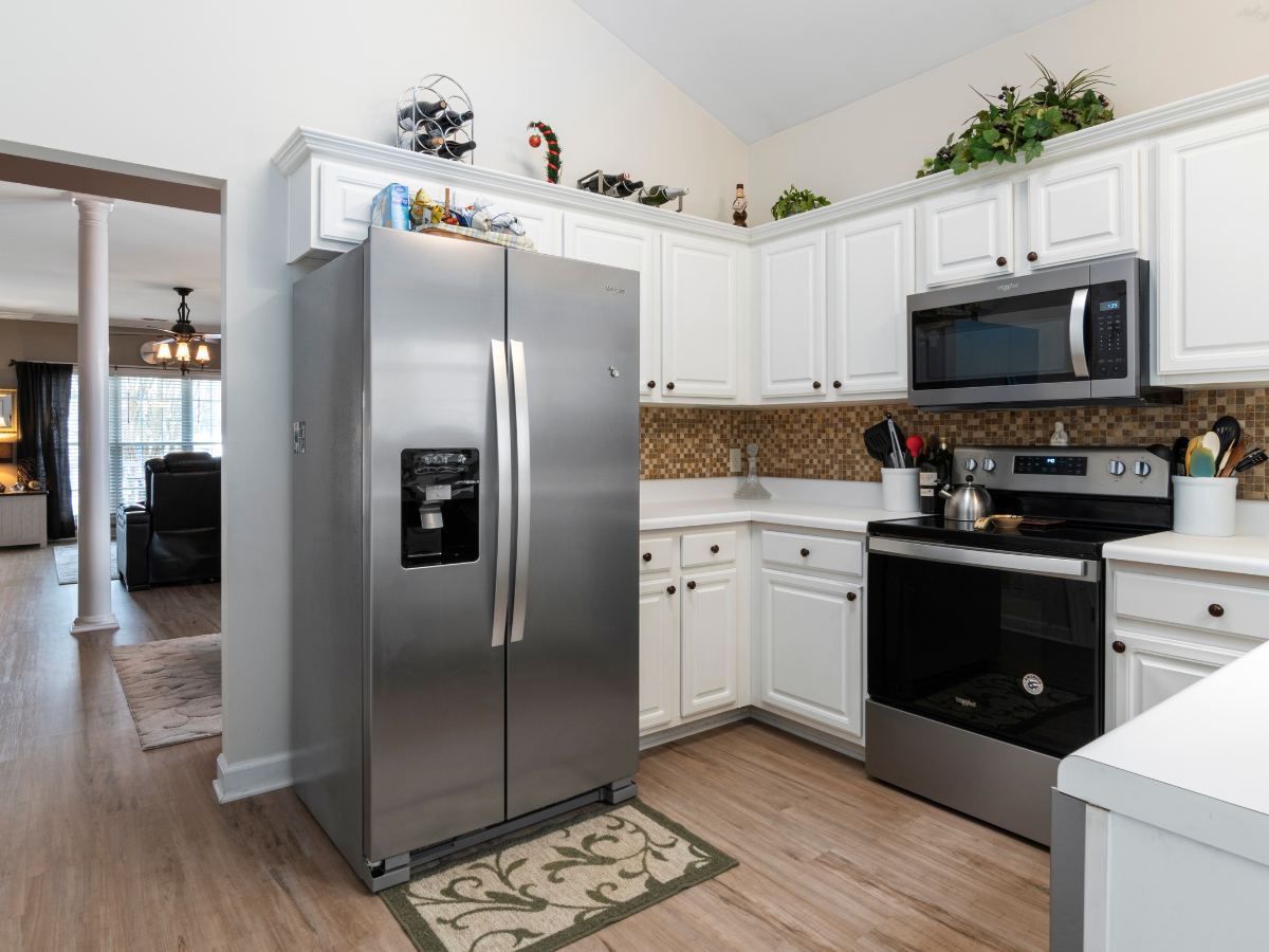 Modern kitchen with energy saving appliances, including a stainless steel refrigerator, oven, and microwave, white cabinets, brown backsplash, and decorative plants on top of the cabinets.