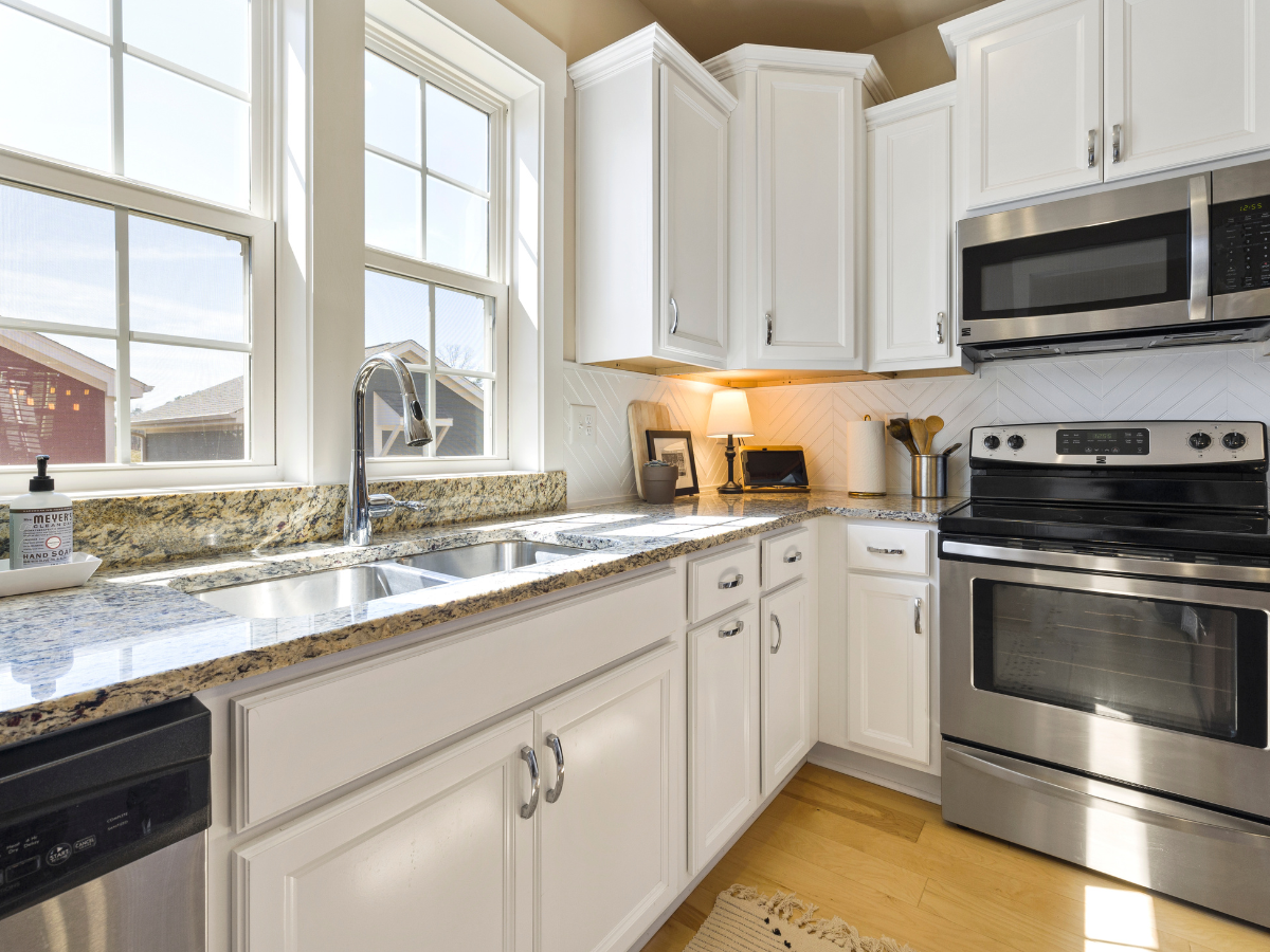 Modern kitchen with white cabinets, granite countertops, energy saving appliances, double sink, and large windows letting in natural light.