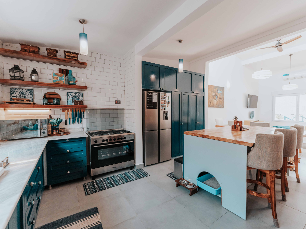 Modern kitchen with teal cabinets, energy saving appliances, open wooden shelves, and a large island with high chairs in a bright, open layout.