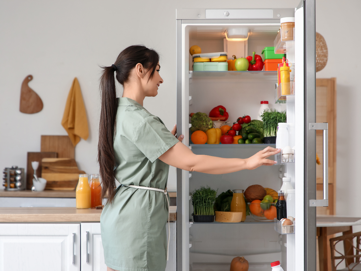 Maximize Space in Your Small Kitchen Today: Expert Storage Ideas and Efficient Layouts 3 Woman in a green dress opens a refrigerator filled with fresh fruits, vegetables, and bottles in a modern kitchen—showing how to maximize space in your small kitchen today.