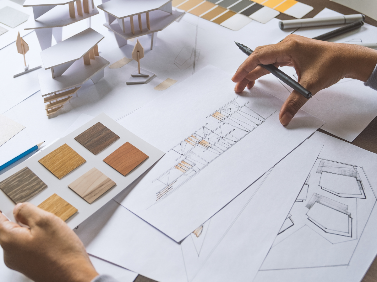 Maximize Space in Your Small Kitchen Today: Expert Storage Ideas and Efficient Layouts 8 Person reviews architectural drawings and wood samples at a desk with model buildings, sketches, and color swatches—planning smart solutions to maximize space in your small kitchen today.