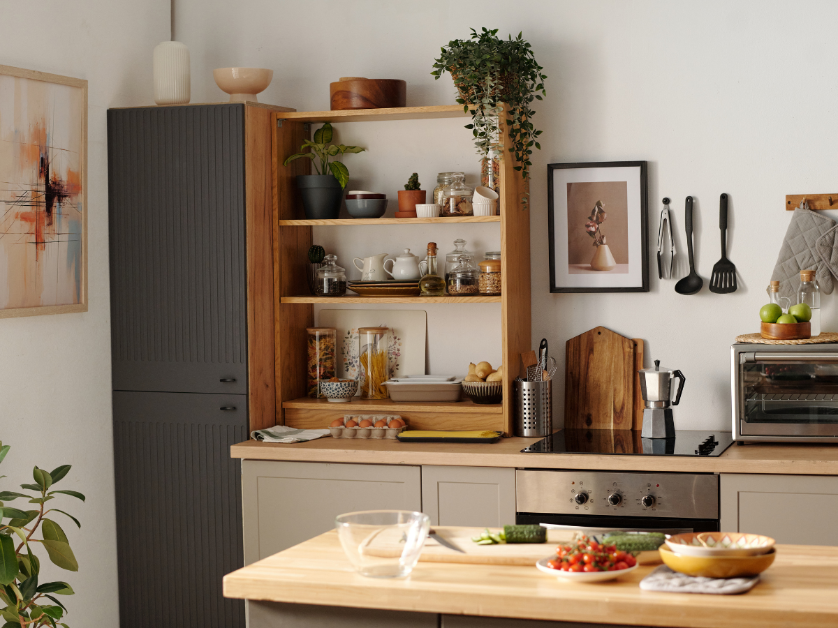 Maximize Space in Your Small Kitchen Today: Expert Storage Ideas and Efficient Layouts 9 Modern kitchen with wooden shelves holding jars, dishes, and plants, a countertop with vegetables and bowls, and utensils hanging on the wall—perfect to maximize space in your small kitchen today.