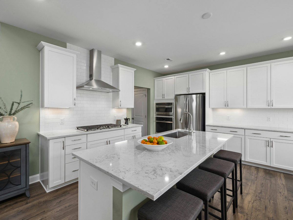 Popular Countertop Color Combinations for White Cabinets in Modern Kitchens 3 Modern kitchen with white cabinets, marble island countertop, stainless steel appliances, bar stools, and a bowl of fruit on the island. Green walls and wooden floor provide stylish combinations for white cabinets.
