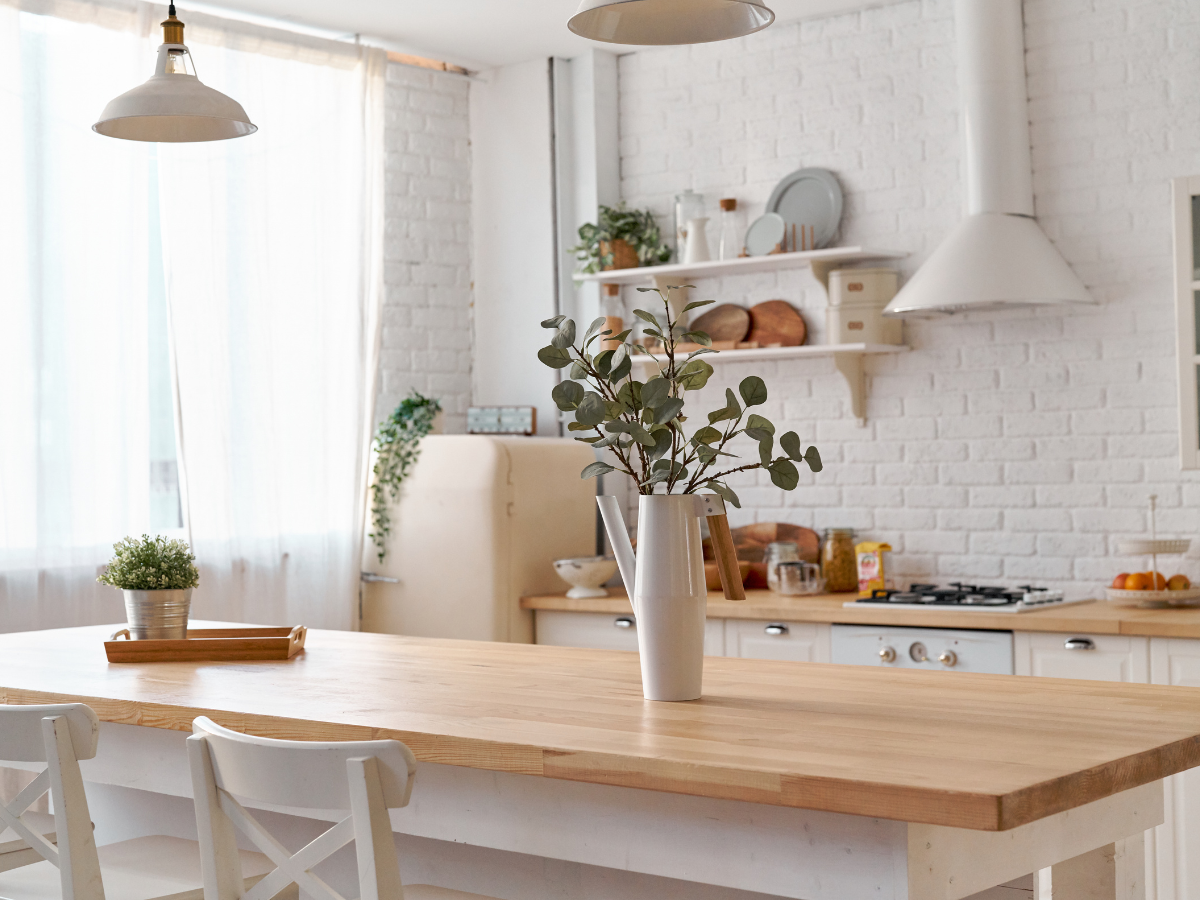 Kitchen Staging Ideas to Wow Potential Buyers: Expert Tips for Effective Home Selling 6 Bright, modern kitchen with white brick walls, wooden countertop, white chairs, potted plants, shelves with dishes, and a vase with greenery on the table—perfect for those seeking fresh staging ideas.