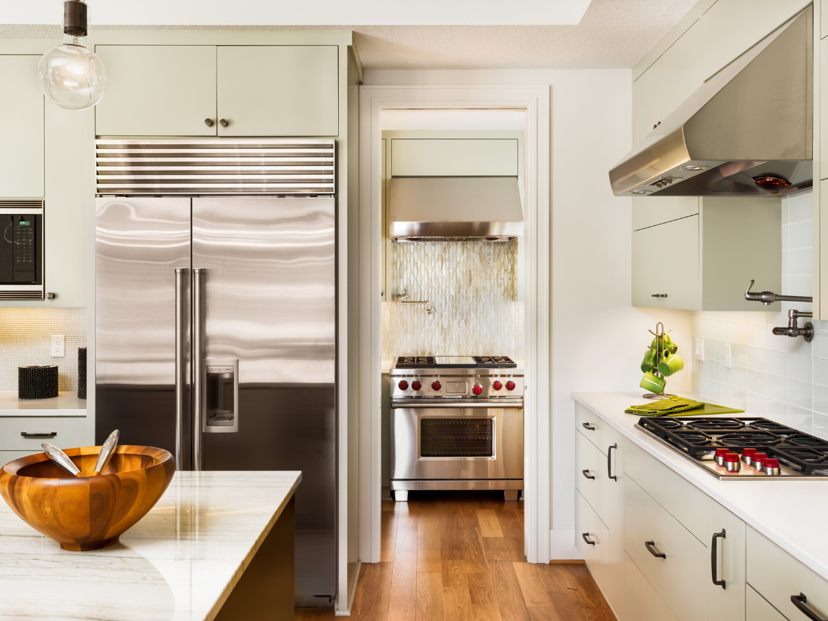 Kitchen Staging Ideas to Wow Potential Buyers: Expert Tips for Effective Home Selling 7 Modern kitchen with stainless steel appliances, light green cabinets, a wooden bowl on a marble island, and a separate cooking area—a perfect layout for those seeking creative staging ideas.