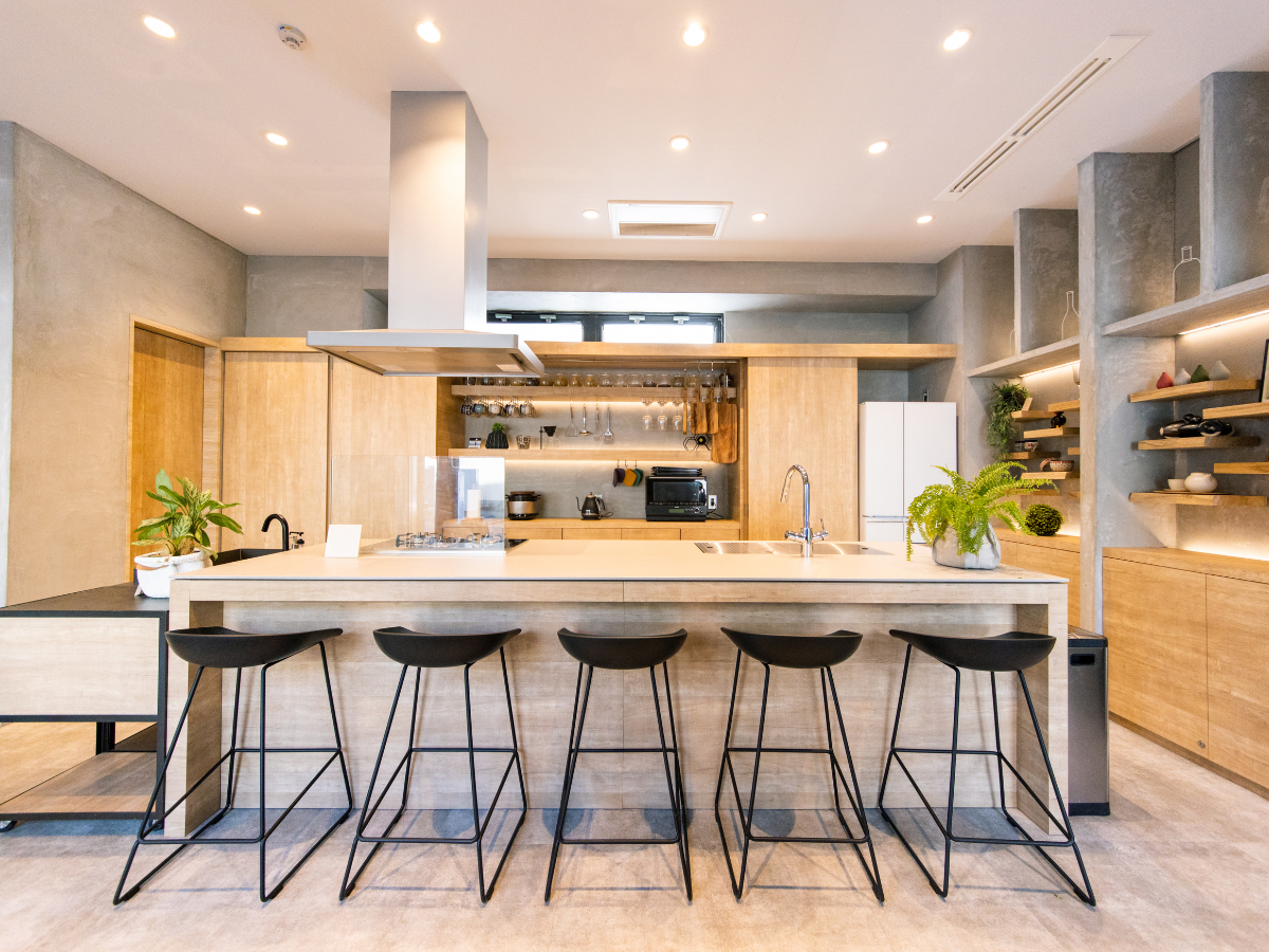 Kitchen Staging Ideas to Wow Potential Buyers: Expert Tips for Effective Home Selling 2 Modern kitchen with light wood cabinets, large island with sink, five black barstools, open shelving, and various kitchen appliances and plants—perfect for showcasing creative staging ideas.