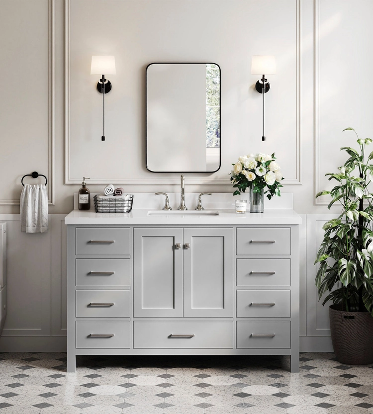 A modern bathroom featuring a gray vanity from ARIEL bath vanities and storage, complemented by a rectangular mirror, twin wall lights, white flowers in a vase, potted plant, hand towel, and a patterned tile floor.