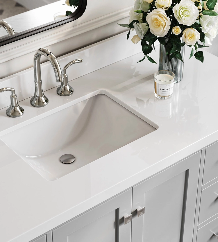 White bathroom sink with silver faucet, gray vanity from ARIEL bath vanities and storage, a glass vase of white and yellow flowers, a candle, and a mirror in the background create an inviting space with stylish cabinetry solutions.