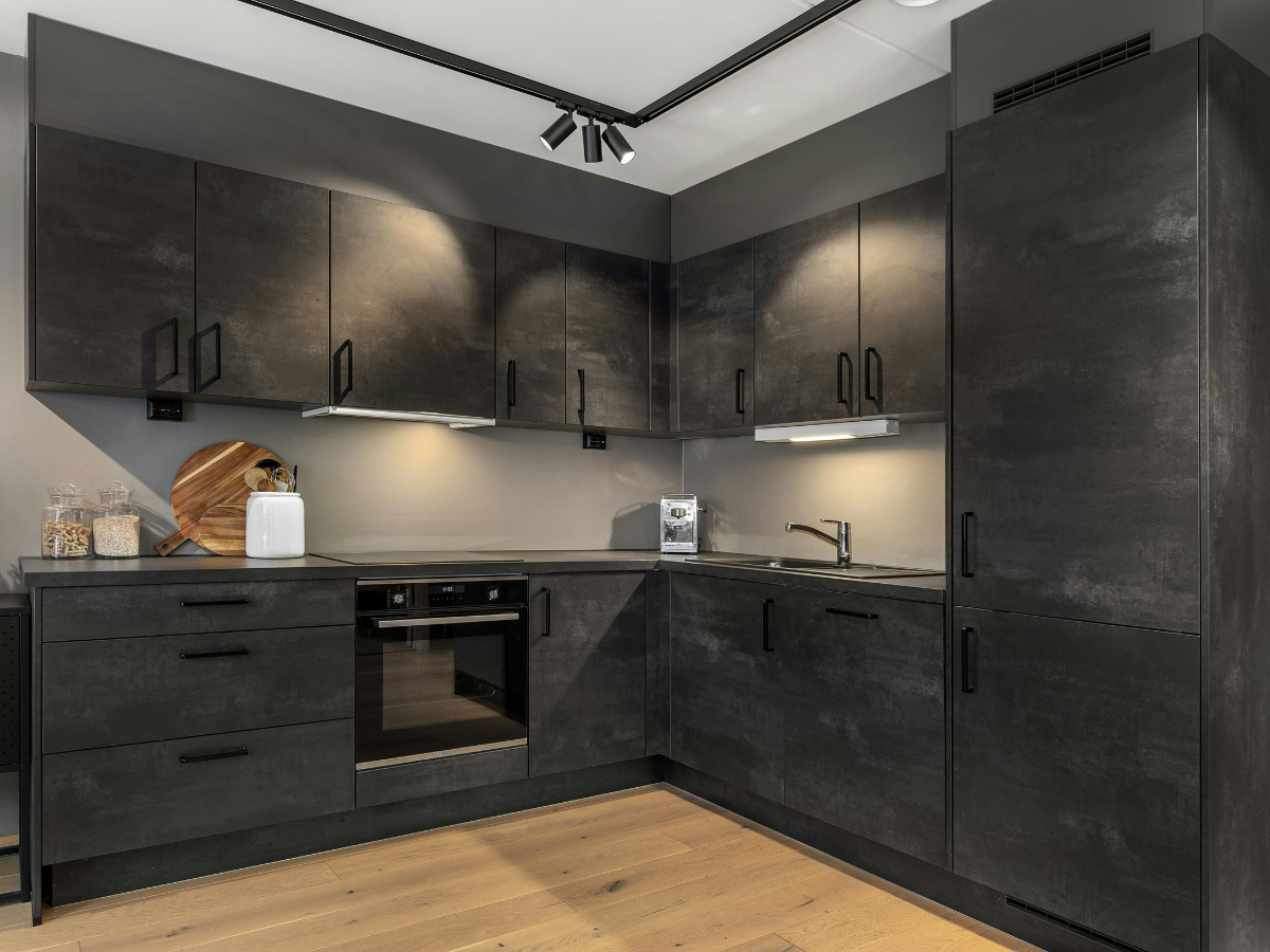 Modern integrated kitchen with matte black cabinets, built-in oven, sink, light wood floor, and small appliances on the countertop.