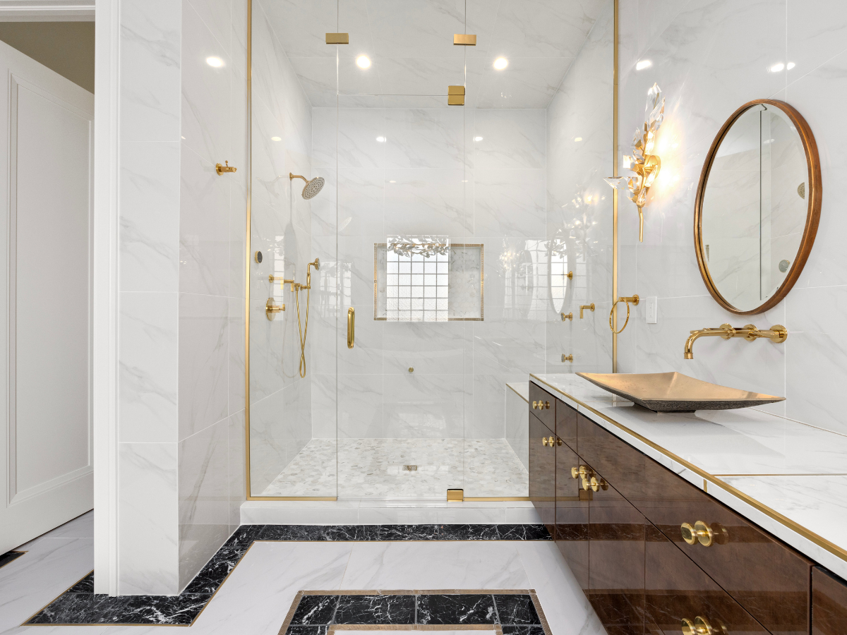 Modern bathroom with marble walls and floors, glass shower enclosure, gold fixtures, vessel sink, round mirror, and wall sconce lighting—perfectly complementing an integrated kitchen for a cohesive home design.