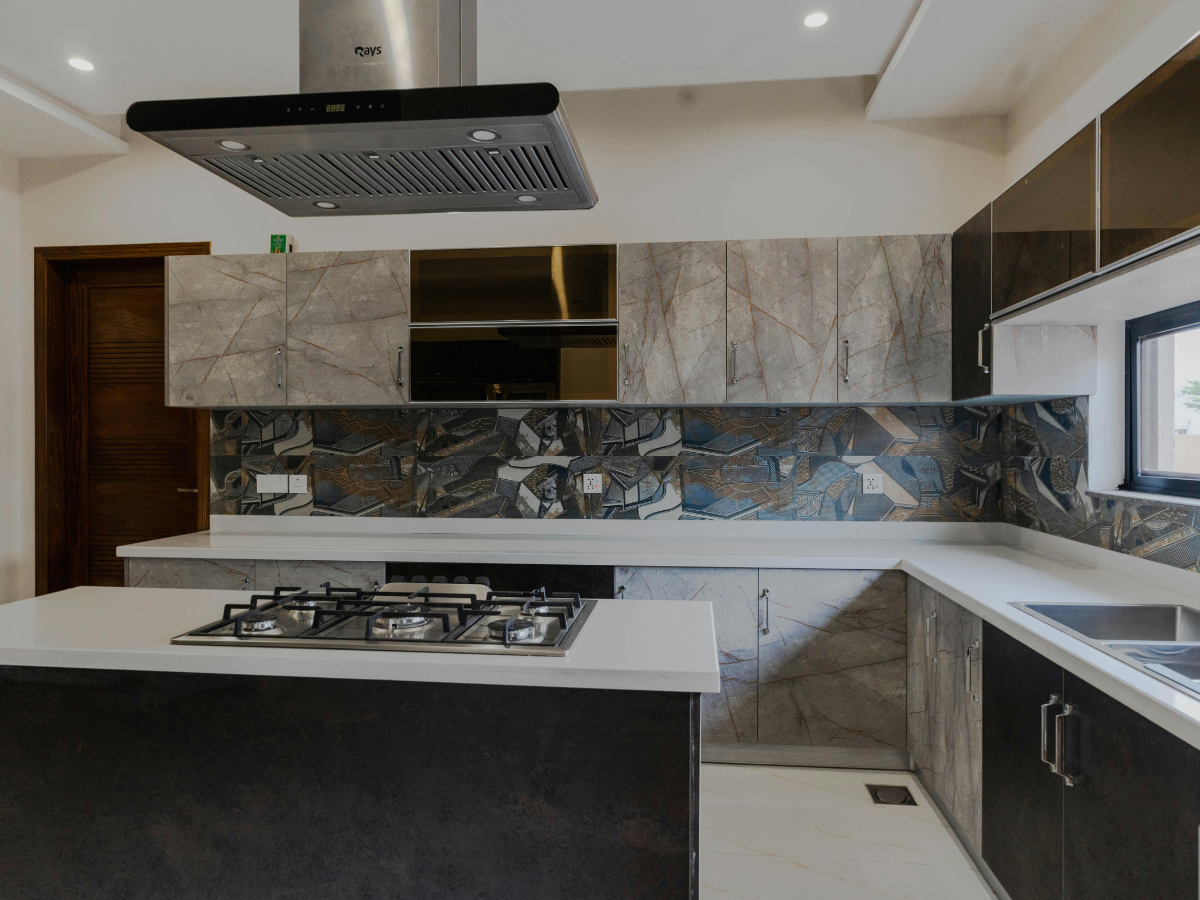 Modern integrated kitchen with marble-patterned cabinets, geometric tile backsplash, a center island with a gas stove, and stainless steel appliances under bright overhead lighting.