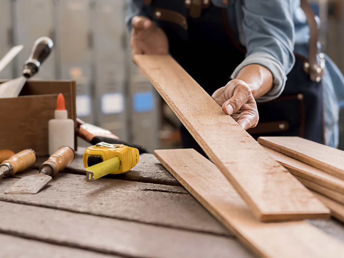 DIY Kitchen Remodeling Tips for a Successful Makeover 4 Person holding a wooden plank on a workbench with measuring tape, glue, and woodworking tools visible in the foreground—perfect for anyone tackling a DIY kitchen remodeling project.