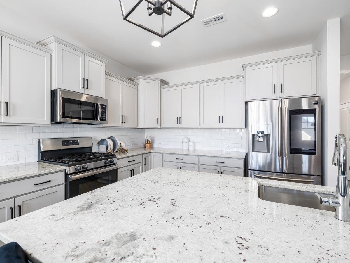 Granite vs Quartz Countertops: Which Is Best for Your Kitchen? 3 Modern kitchen with white cabinets, stainless steel appliances, a gas stove, a double-door refrigerator, and a large granite island countertop with an inset sink—perfect for those debating the benefits of granite vs quartz countertops.