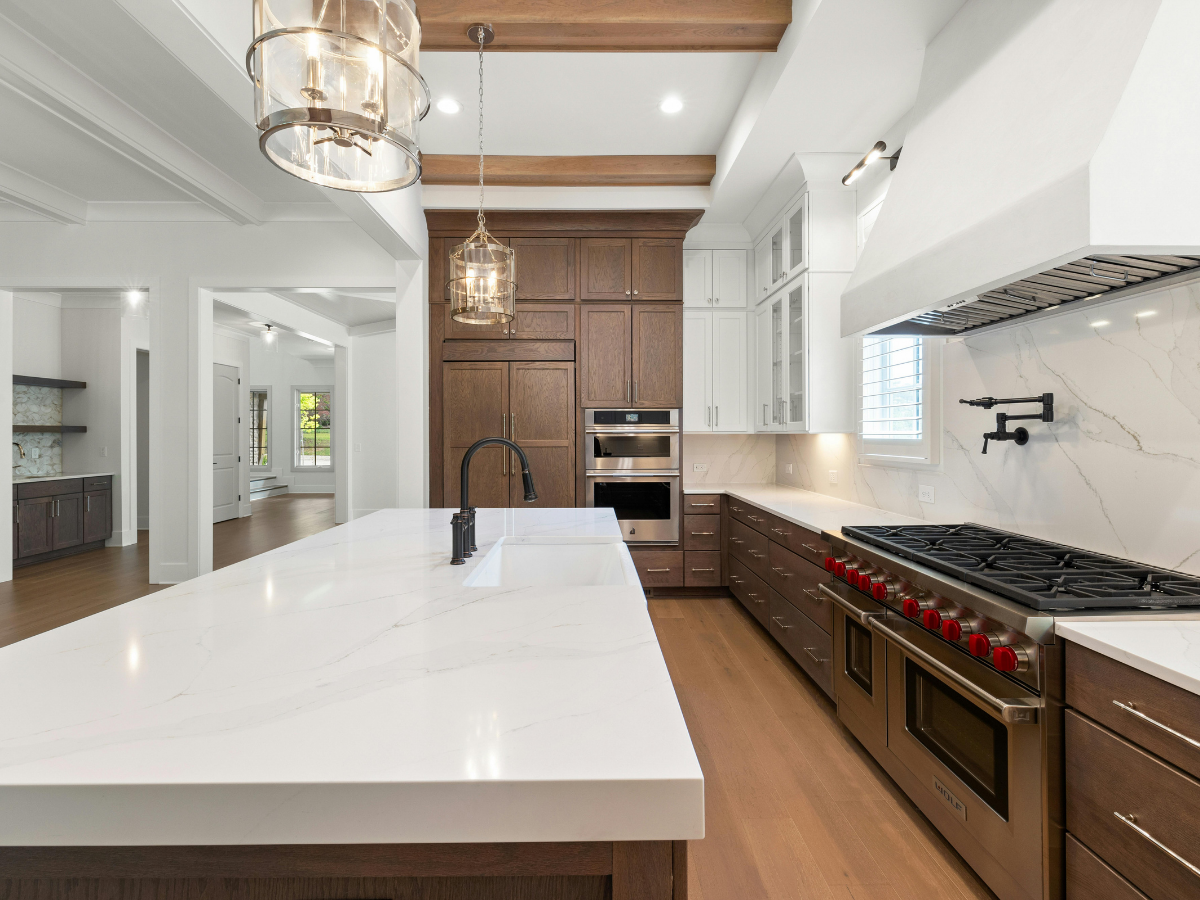 Granite vs Quartz Countertops: Which Is Best for Your Kitchen? 4 Modern kitchen with marble countertops, wood cabinets, stainless steel appliances, gas stove with red knobs, island sink, pendant lights, and hardwood floors—perfect for those exploring granite vs quartz countertops options in contemporary design.