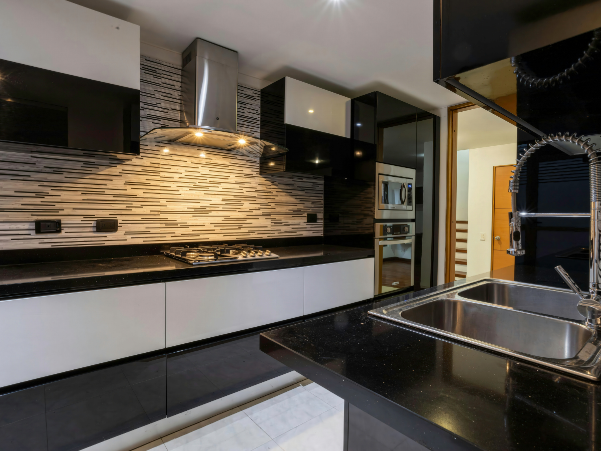 Granite vs Quartz Countertops: Which Is Best for Your Kitchen? 8 Modern kitchen with black and white cabinets, a gas stove under a stainless steel range hood, striped tile backsplash, double sink, and built-in microwave ovens. The spacious layout is complemented by sleek countertops—a perfect setting to consider the advantages of granite vs quartz countertops for both durability and style.